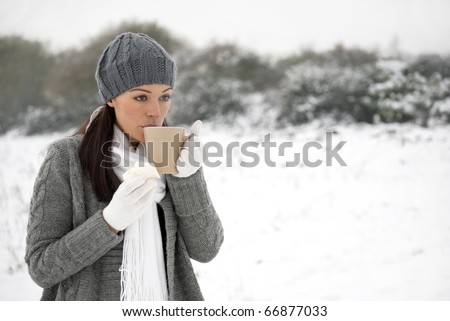Woman blowing on hot drink holding tissue outside in the snow