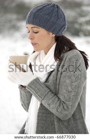 Woman blowing on hot drink outside in the snow