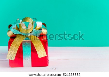 Red gift box and silver ribbons on white wooden and green background, christmas concept.