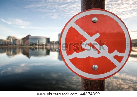A no swimming sign with Tempe Town Lake and downtown Tempe in the background.