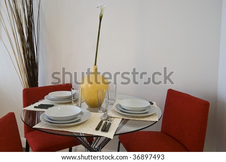 Glas dining table set up with red chairs, yellow vase, plates and cutlery