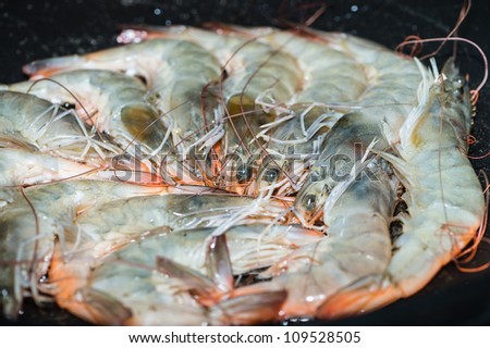 Raw shrimps are cooked on fry pan. Focus on shrimp\'s heads in the middle.