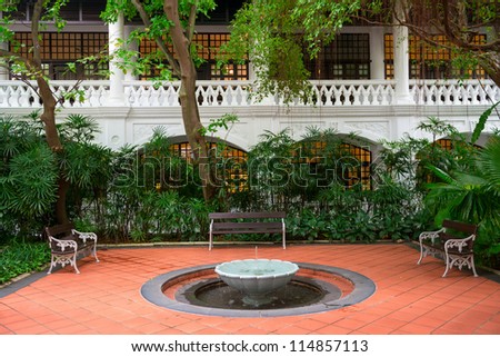 Small fountain in a garden with benches and white classical building on background