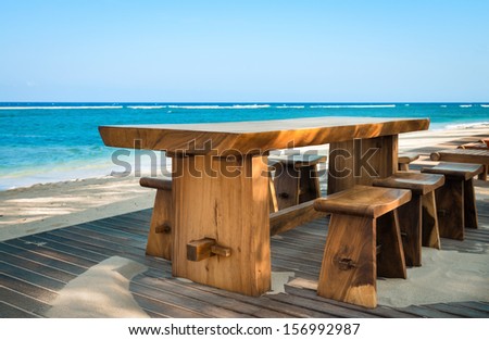 Wooden cafe table and chairs on a tropical beach with blue sea on background