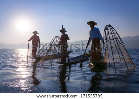 Silhouette of traditional fishermans in wooden boat using a coop-like trap with net to catch fish in Inle lake, Myanmar