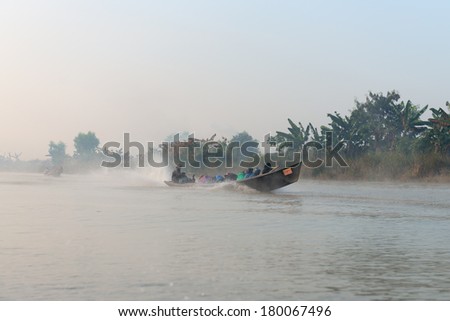 INLE LAKE, MYANMAR (Burma) - 07 JAN 2014: People transportation wooden long boat with motor fast move on blue water in morning fog. Boats is a key transport type on Inle lake.