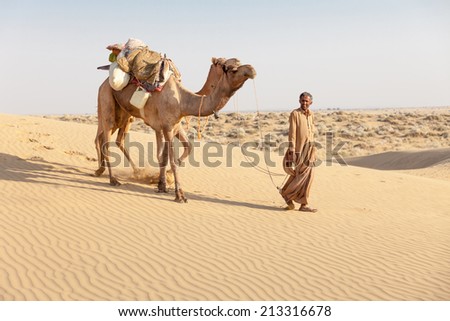 Bedouin and camels in sand dunes in desert under clean sky