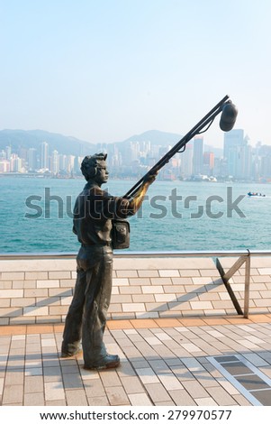 HONG KONG, CHINA - 18 JAN 2015: A bronze statue of a boom mic operator stands on the Avenue of the Stars at Kowloon Promenade, with the Hong Kong skyline in the background.