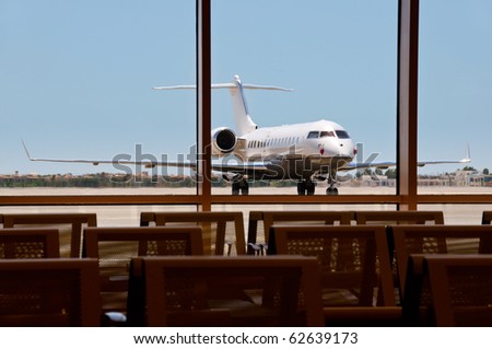 Business plane parked in an airport with seats on foreground. Focus on the plane.