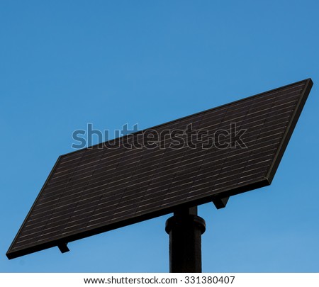 A black solar panel on top of a pole, against a blue sky.