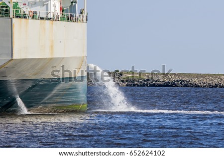 Tanker discharging ballast into the harbor. Water flows from the side. Ship not identifiable. Only part of ship visible.