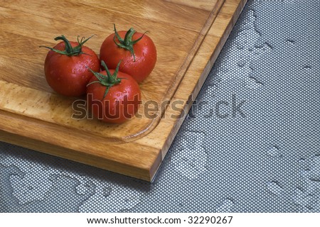 Three fresh tomatoes in the kitchen. Chopping board.