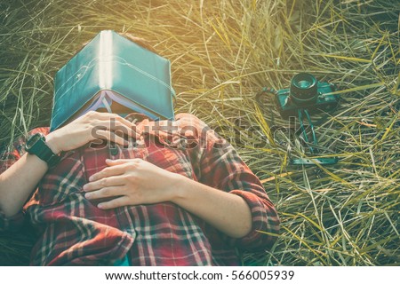 hipster man lying down on grassland napping tired after reading book with nature around outside
