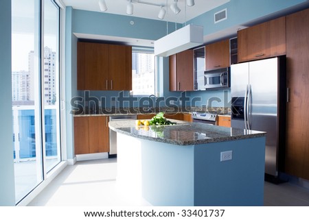 New modern kitchen interior with island in a condo apartment. Brightly lit, light blue walls, granite counter tops, stainless steel appliances. Lemons and fresh salad on the counter top.