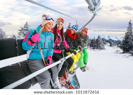 cheerful young friends on ski lift ride up on snowy mountain