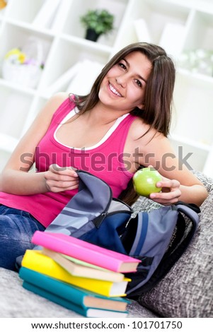 teenage girl packing books for school in book bag at home