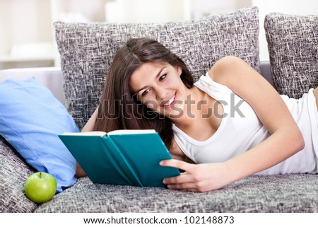 Pretty teen girl reading book and lying on couch in living room