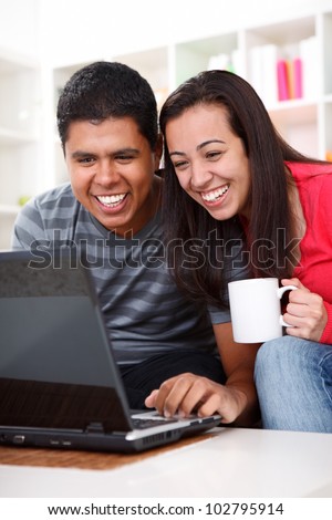 Laughing young couple looking at laptop in home