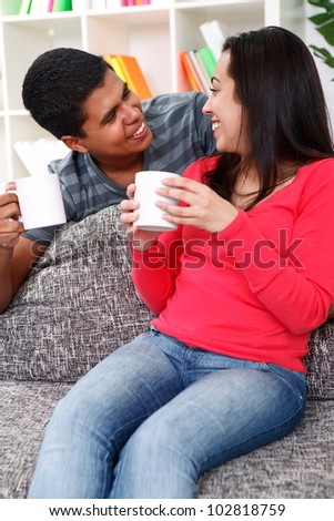 Young couple drinking coffee at home sitting on couch, smiling and looking at each other