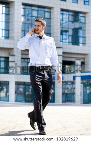 businessman talking on his cellphone while walking outdoors in front of a modern office building