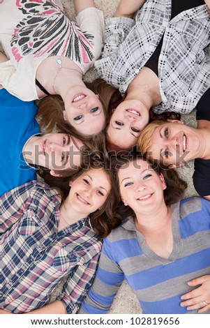 Group of 6 teenagers lying on the floor head next to head, they\'re looking at camera and smiling
