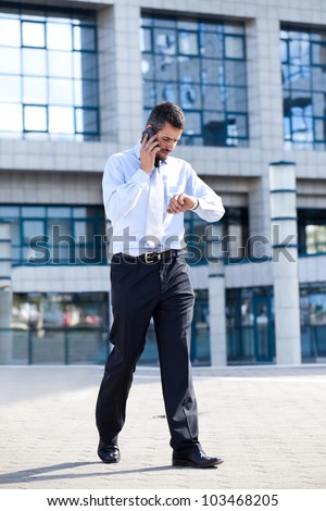 businessman on  phone and checking his watch in front of his office building, running late