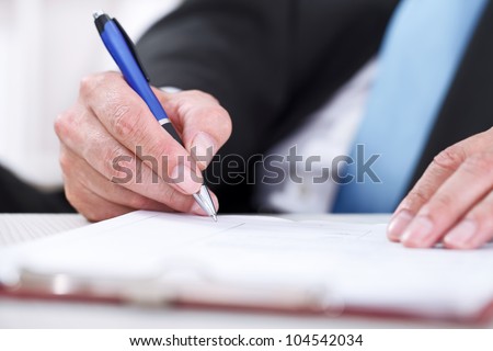 Businessman sitting at office desk signing a contract with focus on signature.