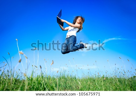 Woman holding a laptop computer jumping over blue sky