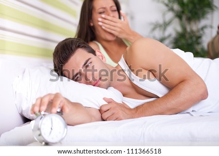 Couple in bed waking up, the men switches off the alarm clock