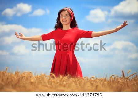 Young woman with hands raised up in the wheat field over blue sky in summer