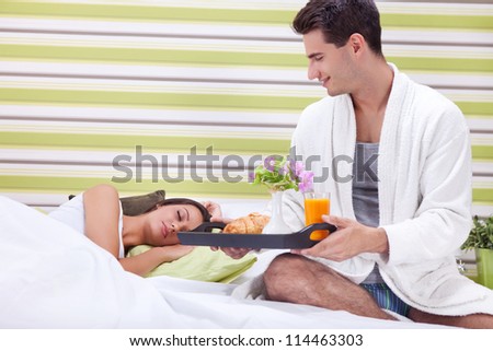 Young man bringing breakfast in bed his sleeping wife