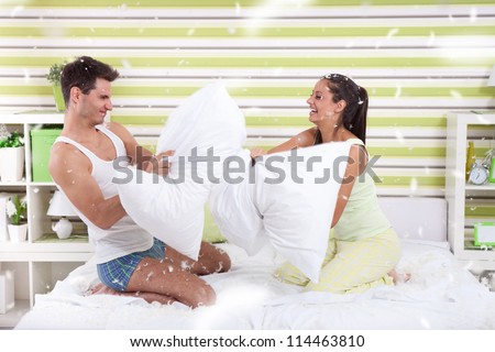 Young couple having fun with pillows in bedroom with lot of feathers