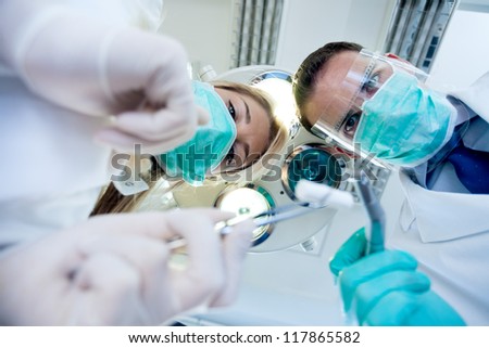 Dental treatment with dentist and dental assistant, from patient\'s perspective, they have drills and angled mirrors