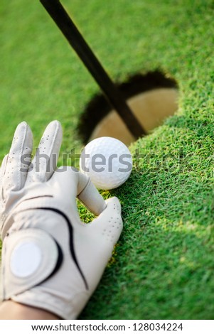 Hand with golf gloves cheating, pulling the ball into the hole