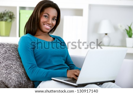 Young Black Girl With Laptop Computer, Sitting In Bright Living Room, Looking At Camera.