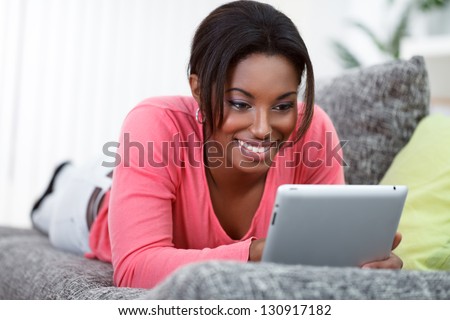 African young woman lying on sofa and using digital tablet