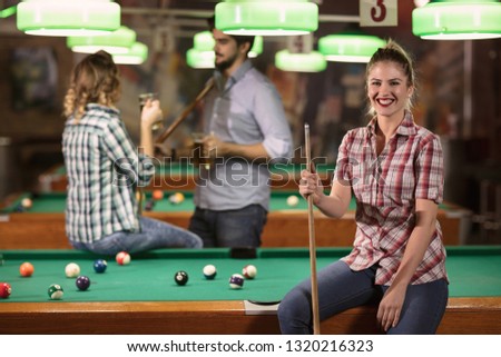 Young smiling girl in billiard club with cue stick posing