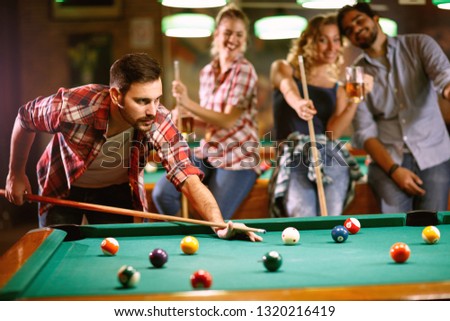 Young handsome man playing billiard game with friends