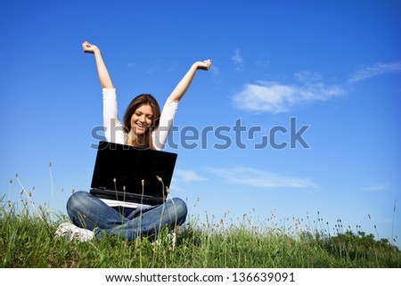 Happy woman with raised arms at a laptop, outdoor