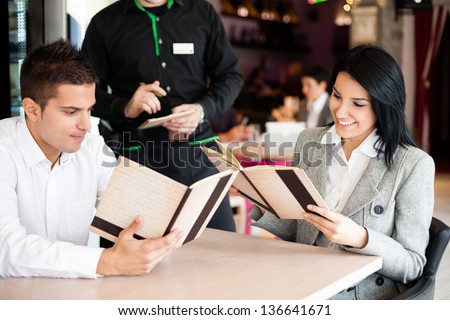 smiling couple orders a meal from a waiter in restaurant