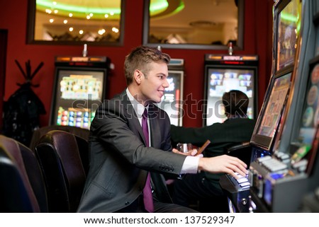 Happy man gambling on slot machine in casino
