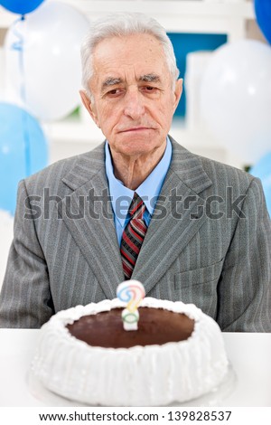 Senior man sitting front of birthday cake with candle in the form of questionnaires