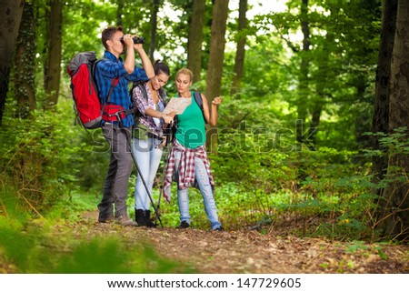 Group of hikers in forest searching right direction with map and binocular