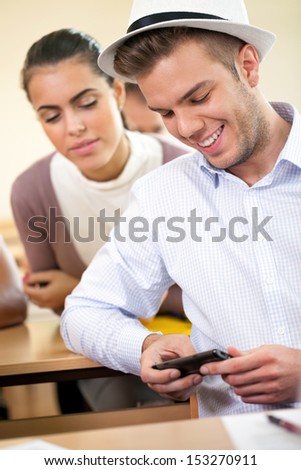 Male student smiling and using smart phone in classroom