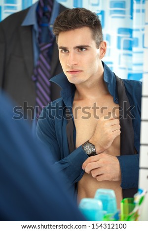 Sexy young businessman getting dressed in the morning with reflected at mirror