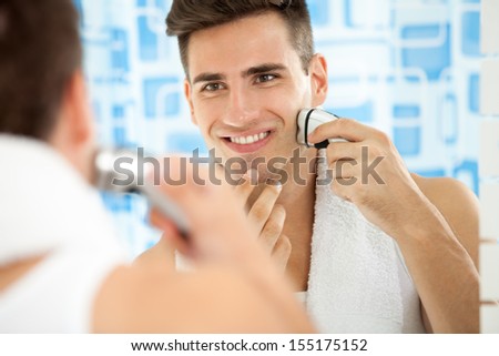 Reflection of young man in mirror shaving with electric shaver