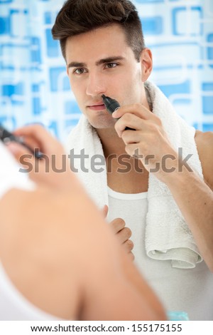 Young man remove hair from his nose with trimmer