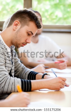 male college student sitting in a classroom and making notes