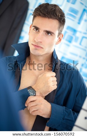 young businessman getting dressed front of mirror in bathroom