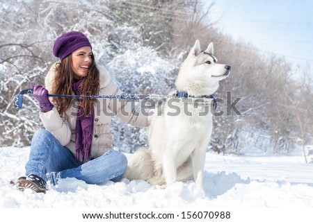 young beautiful woman sits with husky dog in the winter forest